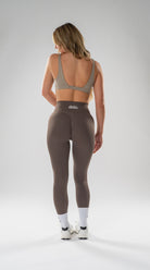 A woman is shown from behind wearing high-waisted athletic leggings and a matching sports bra, standing against a light gray studio background.